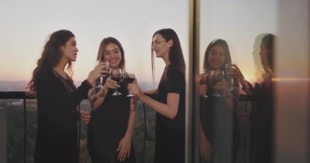 Drie charismatische dames in de top van het gebouw op de balkon drinken wijn en chatten met elkaar — Stockvideo