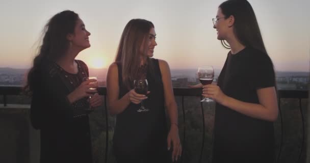 Усміхнені великі дами на вечірці на горищі пентхауса, на балконі з дивовижним видом на захід сонця вони п'ють скляне вино і спілкуються . — стокове відео