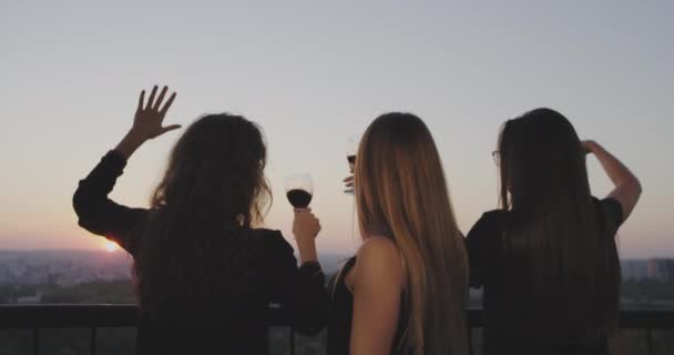 На вершине здания с удивительным видом на закат дамы устраивают винную вечеринку, любуясь красивым закатом и веселясь бокалом вина . — стоковое видео