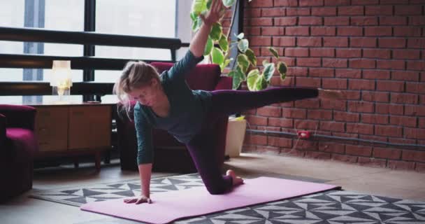 Gyorsított hölgy gyakorló jóga gyakorlatok otthon a nappaliban, ő visel egy kényelmes sportruházat, a szőnyegen. 4k — Stock videók