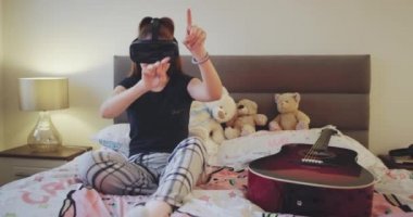 Sanal gerçeklik ile oynamaya hevesli genç gözlük yatak odasında yatağın üzerine döşeme ve bir pijama giymiş, çok karizmatik, oyunu.