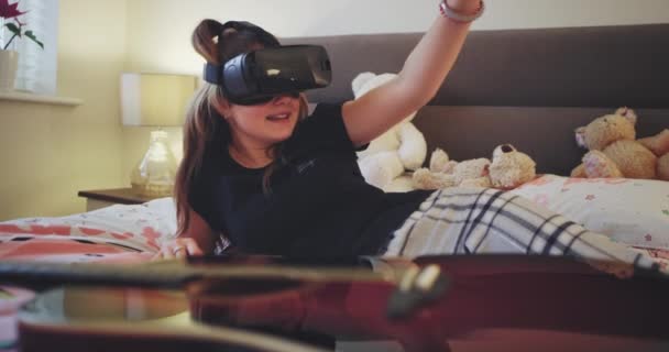 En una habitación para adolescentes moderna, la bella dama juega con unas gafas de realidad virtual que exploran el mundo virtual, se acuesta en la cama y usa ropa de hogar. 4k — Vídeos de Stock