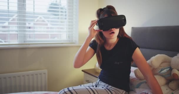 Primer plano de una joven adolescente con gafas de realidad virtual para explorar el mundo muy entusiasta disfrutó del tiempo en su cama y usar una ropa de hogar. — Vídeo de stock