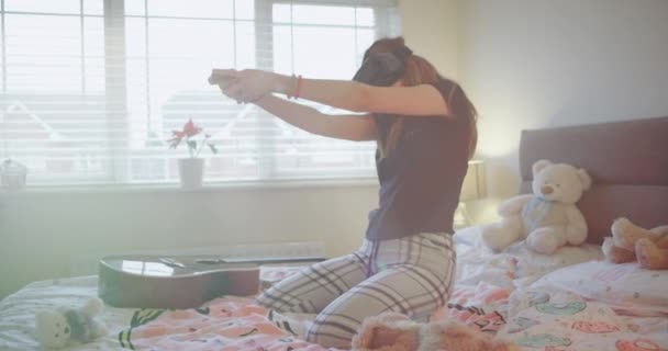 Carismático jovem adolescente usando um óculos de realidade virtual para se divertir em sua cama de pijama ela jogando entusiasta com um VR — Vídeo de Stock