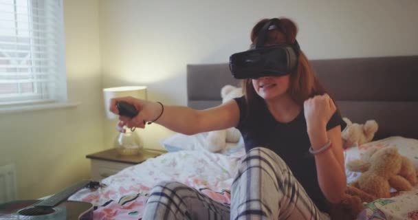 新发明的虚拟现实眼镜少女玩一个新的虚拟游戏在她的卧室, 穿着舒适的睡衣. — 图库视频影像