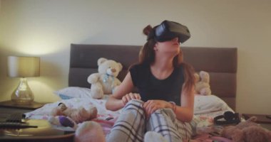 Şirin kız genç odasında bir pijama giymiş ve sanal gerçeklik gözlük yeni bir buluş keşfetmek o çok etkilendim buluş ve mutlu yeni teknoloji keşfetmek.