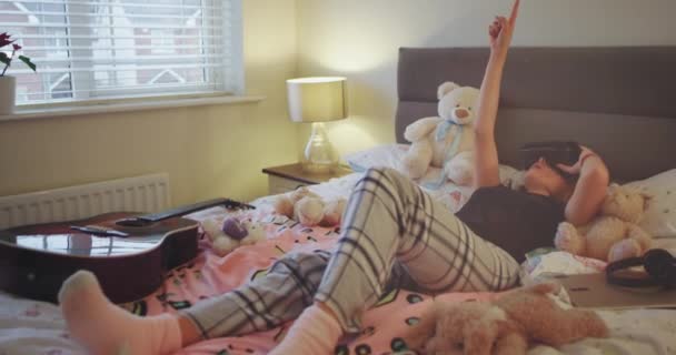 In een tiener kamer meisje op het bed vaststelling dragen van een pyjama's ze verkennen de wereld met behulp van een vr-bril. — Stockvideo