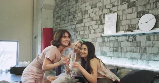 Em um quarto moderno loft multi étnicas jovens senhoras em pijama têm uma festa do pijama, beber champanhe e assistir filme no caderno . — Vídeo de Stock