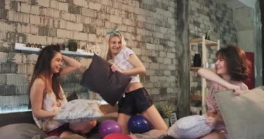 Modern bir yatak odasında bir pijama partisi gecesi çok etnik bayanlar var eğlenceli bir zaman birlikte dayak ile yastık, onlar büyük ve duygu büyük gülümseyen.