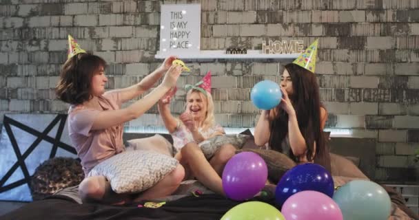 На дне рождения в кругу друзей девочки-подростки играют с воздушным шаром в современной спальне и в забавной шляпе на день рождения они проводят большое время вместе. 4k — стоковое видео
