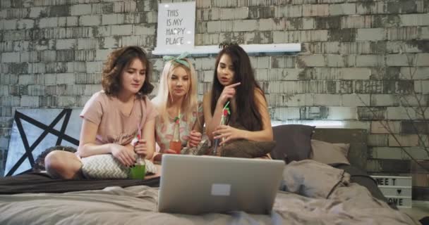 Tierfreunde Teenie-Ladys feiern eine Sleepover-Party, auf dem Bett sehen sie eine Komödie auf dem Notizbuch, lächeln und plaudern miteinander, halten eine Flasche mit etwas Getränk in der Hand. — Stockvideo