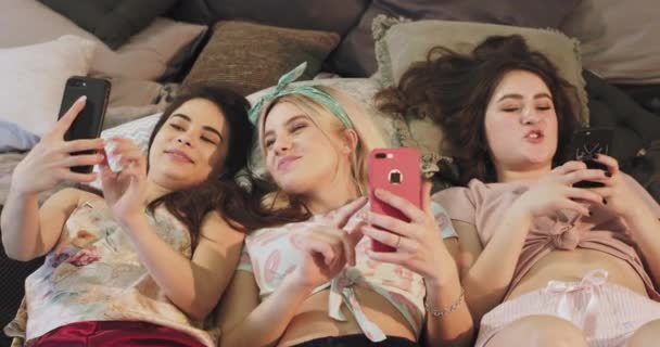 Mooie tiener dames in een homewear kleding met behulp van een smartphone, terwijl tot vaststelling van op het bed, eten kauwgom en het gevoel gelukkig. — Stockvideo