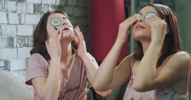 Beaty time for a young ladies in the morning have a routine for a face make a eye mask from cucumber in pajamas. — Stock Video