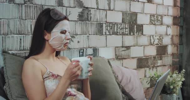 Eine Geschäftsfrau hat eine Beauty-Routine, bevor sie mit einer Gesichtsmaske zur Arbeit geht und an einem Laptop arbeitet und einen heißen Kaffee trinkt — Stockvideo