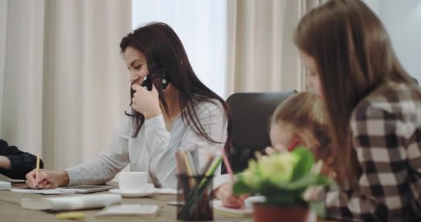 Por la mañana, la mujer madura acelera el tiempo con sus hijos antes de la escuela, habla por teléfono bebiendo café y revisando la tarea. 4k — Vídeo de stock