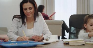 Büyük bir masada otururken, bir tablet kullanarak ödev yapmak için onlara yardımcı üç çocuk ile modern Anne, onlar iyi bir ruh hali var ve olgun anne ile büyük bir zaman hız