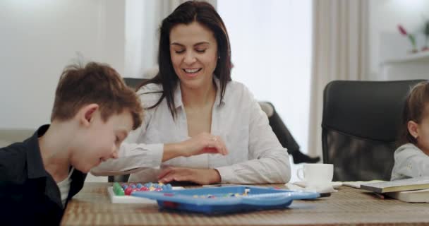 Úžasná dospělá matka pomáhající svým dětem dělat školní projekt, sedí v moderním obývacím pokoji s velmi koncentrovanou atmosférou, babička čte knihu na pohovce. — Stock video