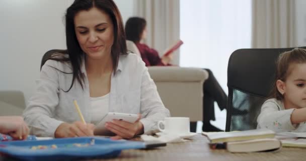 Moderne moeder met haar drie kinderen hen te helpen om huiswerk te doen met behulp van een Tablet, zittend op een grote tafel, ze hebben een goed humeur en het versnellen van een geweldige tijd met de volwassen moeder — Stockvideo
