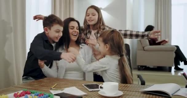 Una relazione amichevole tra la madre e i suoi tre figli si abbracciano molto bene in una casa moderna, mentre la nonna siede sul divano e legge un libro . — Video Stock