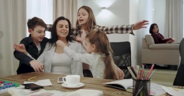 Sehr charismatische reife Mutter mit ihren drei Kindern bilden ein freundschaftliches Beziehungsteam, sie umarmen sich liebevoll und verbringen eine schöne Zeit zusammen in einem modernen Wohnzimmer. — Stockvideo