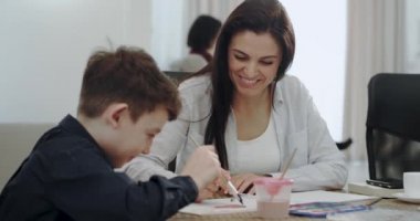 Modern bir evde çocukları ile birlikte ev ödevi ve bazı el sanatları zaman harcama ile olgun bir anne, arka plan büyükannem kanepede otururken bir kitap okuma.