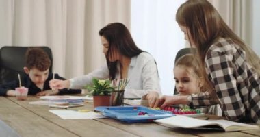 Büyük bir aile üç çocuk ve güzel bir olgun anne birlikte büyük bir mutfak masası boyama bir zaman harcamak ve bir masa oyunları arka plan büyükannem bir kitap okuma var. 4k