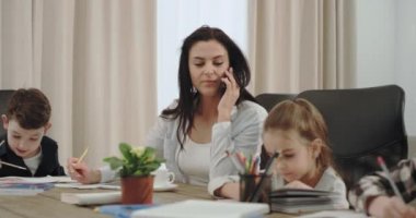 In a modern house businesswoman and mature mother speaking on phone while doing home with her three children , on the sofa background grandmother reading a book.