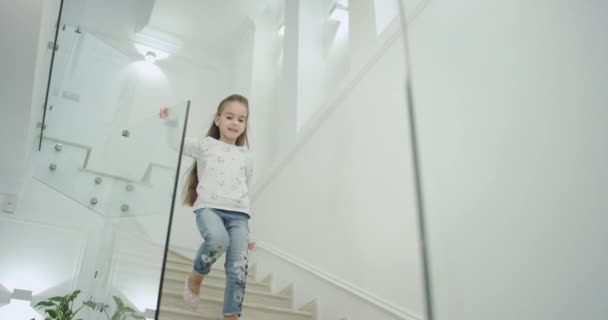 Een klein meisje zes jaar oud in de ochtend in een modern huis ontwerp trap ze naar beneden naar de eerste verdieping. — Stockvideo