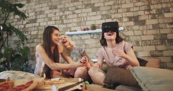 Three young ladies speeding a good time at sleepover , in pajamas laying down in the bed , one of the lad using a virtual reality glasses very enthusiastic using different programs , other ladies — Stock Video