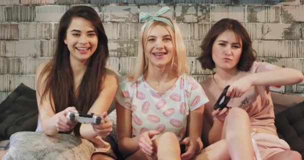 Trzy Nastolatki Panie grając na PlayStation gry przed kamerą na noc sleepover party, w piżamie robią śmieszne twarze i dostać skoncentrowany do gry — Wideo stockowe