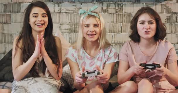 En un moderno grupo de dormitorio de amigas señoritas jugando en un videojuego de PlayStation frente a la cámara muy impresionadas se concentraron en el juego, en pijama se apresuraron un rato divertido juntas — Vídeo de stock