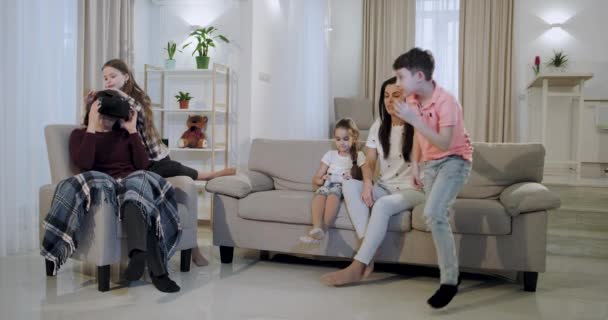 Czas rodzinny dla dużej rodziny odkrywania nowej technologii wirtualnej rzeczywistości okulary wnuki wprowadzenie ich babcia VR wszystkie siedzą na kanapie w dużym przestronnym salonie. — Wideo stockowe