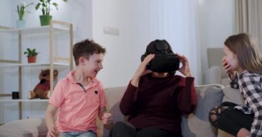 Yakın çekim kanepede torunları ile birlikte vakit geçiren bir büyükanne , çocuklar ilk kez büyükanne bir Vr veren onlar çok komik arıyoruz ve büyükanne etkilendim