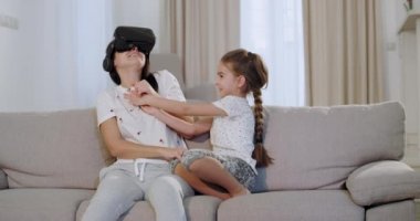 Anne ve kızı kanepede otururken, yeni bir dünya keşfetmek için sanal gerçeklik gözlüğü kullanarak anne birlikte güzel bir zaman harcama