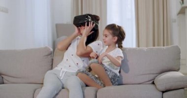 Kanepede otururken sanal dünyayı keşfetmek için yeni bir teknoloji kullanarak olgun annesi ile sevimli bir küçük kız , olgun kadın vr kullanarak çok o etrafa bakarak etkilendim