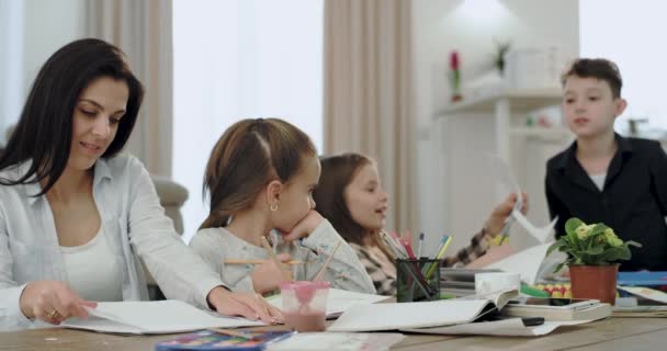 Em uma espaçosa sala de estar uma mãe com três filhos fazendo projeto escolar juntos como uma equipe amigável eles passam um bom tempo juntos — Vídeo de Stock