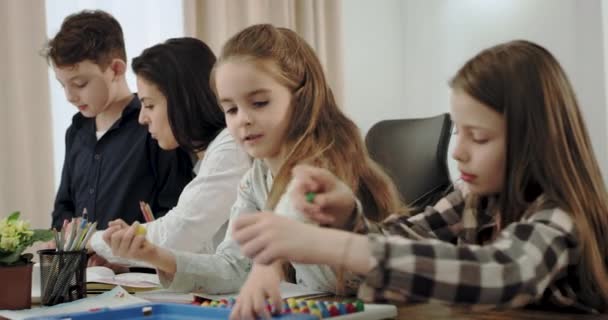 Porträt charismatischer Kinder mit ihrer reifen Mutter, die gemeinsam Hausaufgaben macht und nach der Schule eine schöne Zeit miteinander verbringt, während die Oma im Hintergrund ein Buch liest — Stockvideo