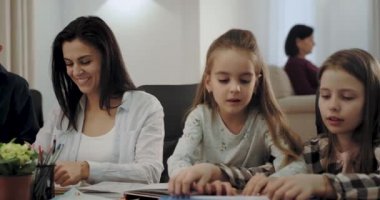 Anneleri meşgul ve bir kitap okuma arka planda büyükanne iken çok sevimli iki kız kardeşi bir masa oyunu birlikte oynarken