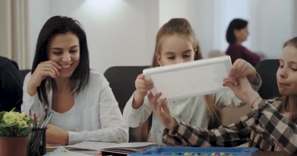 Glimlachend mooie rijpe vrouw en haar drie kinderen zeer charismatisch, ze hebben een geweldige tijd samen na het huiswerk ze samen spelen op een tafel spel zeer geconcentreerd in een ruime woonkamer — Stockvideo