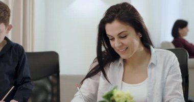 Çocukları ile Awesome olgun anne onlara bazı ev ödevi yapmak için yardım , onlar çok mutlu ve arka planda büyükanne bir kitap okuma kanepede heyecanlı