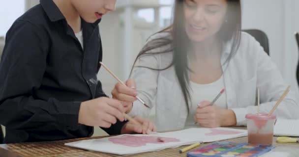 Portret van een volwassen vrouw tijd doorbrengen met haar zoon samen te schilderen voor een school project, zeer aantrekkelijke mensen in een modern huis — Stockvideo