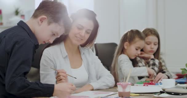 En una gran sala de estar espaciosa después de la escuela madre con sus tres hijos haciendo un proyecto escolar de la tarea muy concentrado y emocionado — Vídeo de stock