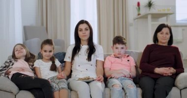 Kanepede büyük bir geniş oturma odasında anne ve büyükanne ile mutlu çocuklar kamera önünde tv eğlenceli bir şey izlerken onlar gülümseyen bir yüzleri var