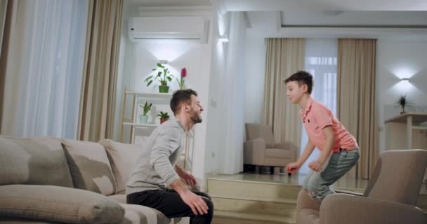 Big Brothers spędzają czas z małym bratem w salonie cute Boy skoki do jego wielkiego brata, podczas gdy siedzą na kanapie — Wideo stockowe