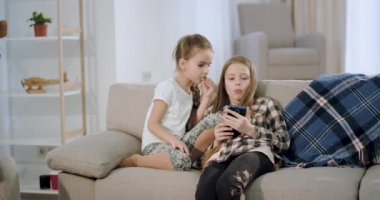 Konsantre iki küçük kız kanepede otururken bir akıllı telefon kullanarak birlikte bir video oyunu oynarken eğlenceli bir zaman var
