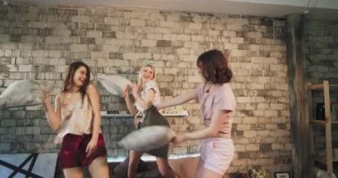 Bir grup genç için closeup komik zaman onlar yastık ile dayak yatakta modern bir yatak odasında pijama bir yatıya parti var