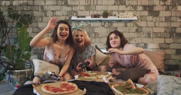 Πολύ χαμογελαστοί και χαρισματικές κυρίες πολλαπλών εθνοτικών παιχνίδι σε έναν ΠΥΠ μπροστά από την κάμερα στο μοντέρνο υπνοδωμάτιο τρώγοντας πίτσα και περνώντας μια καλή στιγμή — Αρχείο Βίντεο