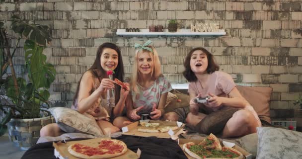 Мультиэтнические девушки-подростки на ночевке играют на PSP на кровати во время еды пиццы, очень воодушевлены они играют сосредоточены, одеты в пижаму — стоковое видео