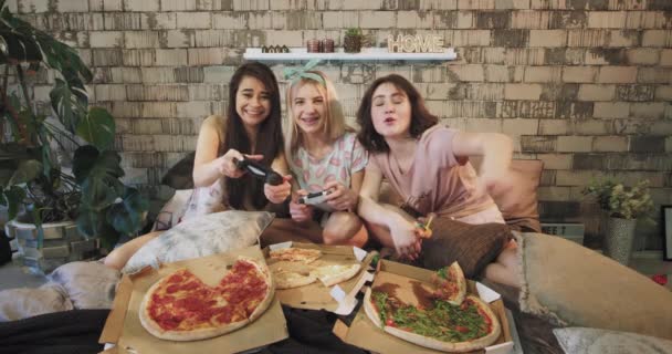 Di depan kamera tiga wanita muda bermain multi etnis pada PSP yang sangat terkonsentrasi dan antusias, di pesta menginap sambil makan pizza dan minum koktail — Stok Video
