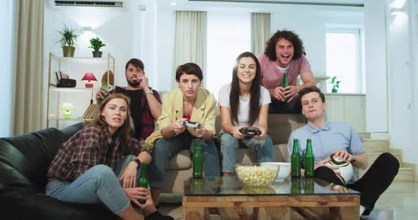 A big group of friends ladies and man very attractive have a good time together playing on the front of TV in a video game while drinks some beer they have a very exciting time together — Stock Video